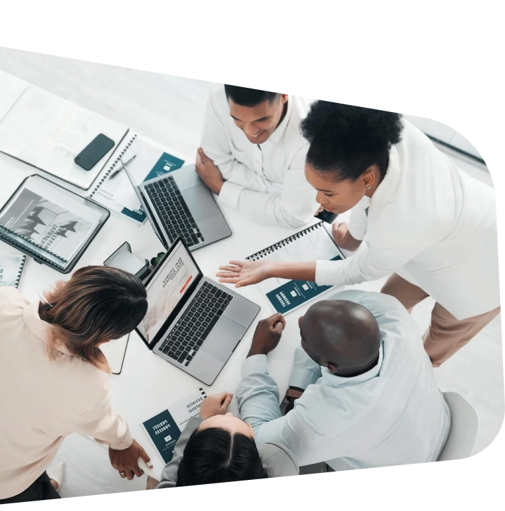 A diverse group of colleagues gather around a table, collaborating intently over laptops and documents, exuding teamwork and focus.