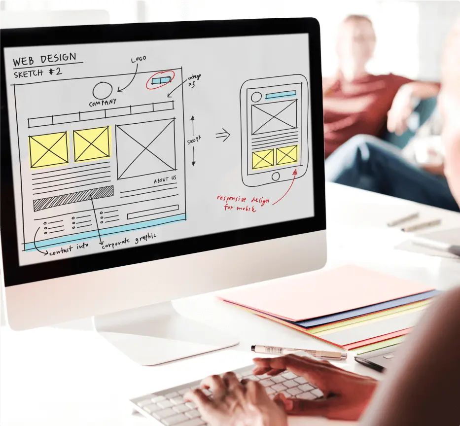 A person works on a computer displaying a web design sketch. The screen shows desktop and mobile layouts, highlighting responsive design concepts.
